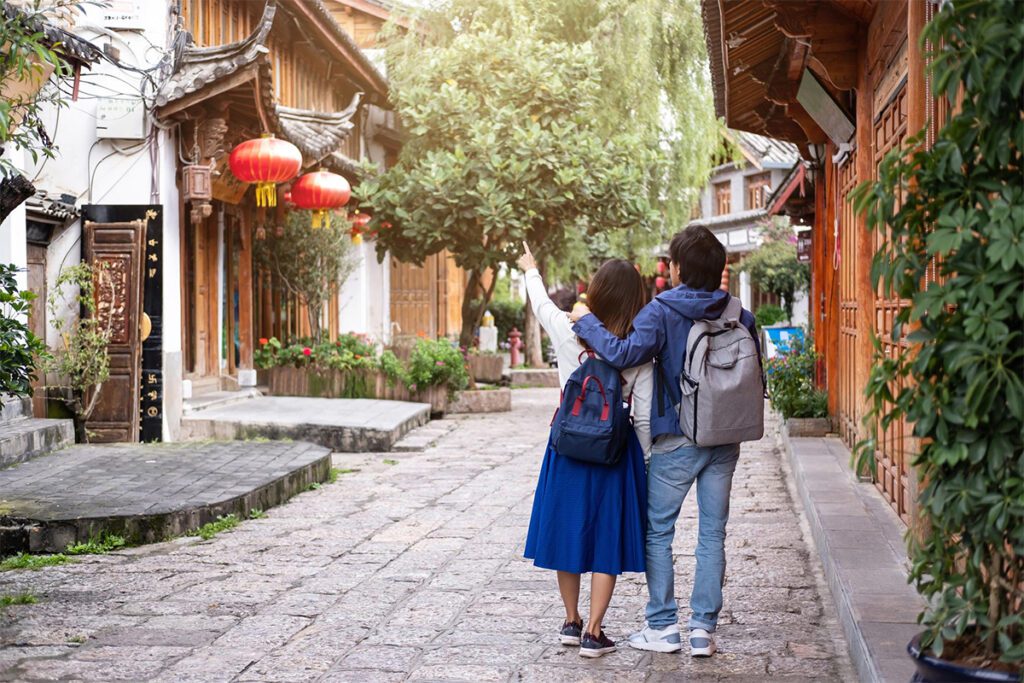 เคล็ดลับการท่องเที่ยวในคุนหมิง ดาลี และลี่เจียง 昆大麗旅遊注意事項:旅客漫步於昆明、大理、麗江古城的傳統街巷,兩旁可見木造建築、石板路與紅燈籠,呈現雲南古城悠閒的旅遊氛圍,適合用於昆大麗旅遊注意事項與自由行攻略內容。