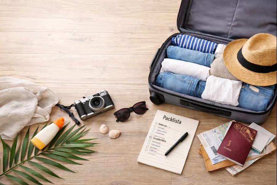 kunming dali lijiang travel packing checklist 敞開的行李箱內整齊排列著衣服與草帽,旁邊放有相機、太陽眼鏡、護照及旅遊打包清單