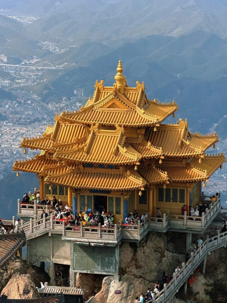 lijiang laojushan golden pavilion mountain top 麗江老居山景區金頂,雄偉金色道觀矗立於山巔岩石上,遊客聚集於平台,遠方層疊山脈綿延,古建與群山構成仙氣滿滿的山岳風景。