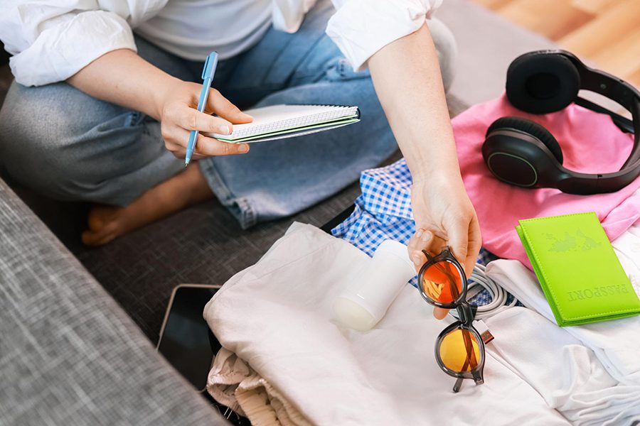 planning yunnan itinerary and packing sun protection 一位坐在沙發上的女子一手拿筆與筆記本紀錄行程,另一手正在收拾琥珀色太陽眼鏡