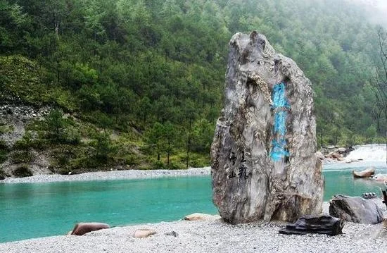 Lijiang Blue Moon Valley 麗江藍月谷湖水呈現清澈的藍綠色,河谷被翠綠山林環繞,岸邊立著刻有「藍月谷」字樣的天然巨石,湖水與森林相互映襯,展現玉龍雪山腳下寧靜而夢幻的自然風景。
