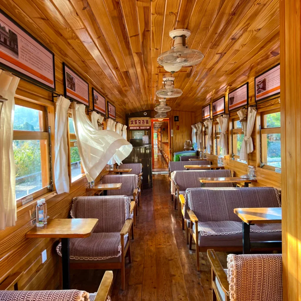 Jianshui Miniature Train 建水小火車復古車廂內部景觀,木質天花板與牆面營造溫暖氛圍,兩側窗戶配有白色窗簾與木桌座椅,車廂內整齊排列的座位與吊扇呈現懷舊鐵道風格,展現建水小火車獨特的歷史與觀光魅力