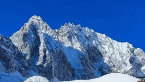 雲南麗江玉龍雪山，雄偉鋸齒狀積雪山峰聳立於澄澈深藍天空下，山腳有小型觀景平台。