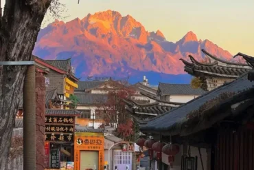 Antica città di Shuhe 1 Un punto panoramico mozzafiato nella città antica di Lijiang da cui ammirare il Monte Yulong: all’alba, la montagna innevata viene illuminata da bagliori dorati e rossastri, creando lo spettacolo naturale della “montagna d’oro illuminata dal sole”, con in primo piano le antiche costruzioni in stile Naxi.
