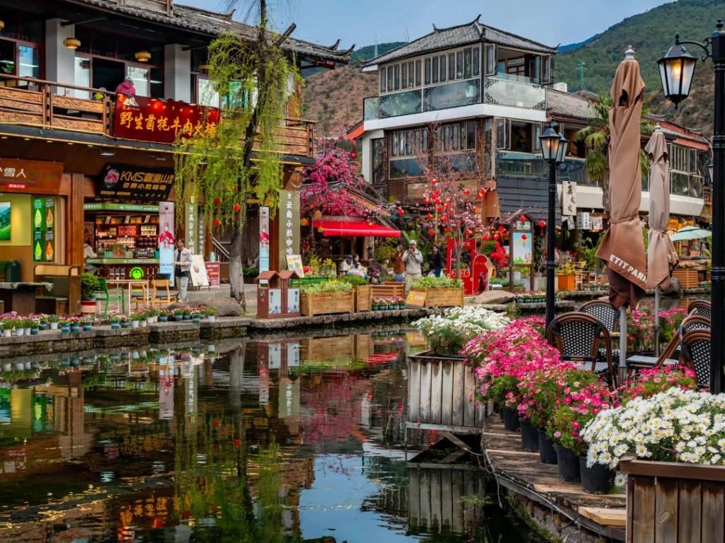 Shuhe Ancient Town 4 麗江束河古鎮的唯美水景,碧綠潭水倒映著翠綠垂柳、鮮豔花卉與古色古香的納西建築,呈現如畫般的夢幻景致。